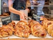 Auslage goldener gedrehter Kanelbulle mit Hagelzucker und Zimt. Ein Kreidetafelschild zeigt 'Kanelbulle 25:-' in einer nordischen Bäckerei.