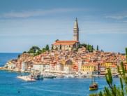 Rovinj, Istria: Colorful coastal town on a peninsula with terracotta roofs, prominent church tower, and boats in the blue Adriatic Sea.
