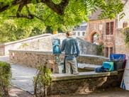 Artist painting on easel by canal in Bruges, Flanders. Stone bridge and historic brick buildings visible in background under green foliage.