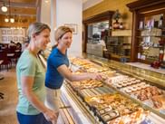 Zwei Frauen betrachten Gebäck im Café Zauner in Bad Ischl. Glastheke zeigt verschiedene Kuchen, Torten und Desserts in traditionellem Café.