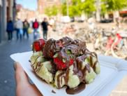 Belgische Waffel mit weißer und dunkler Schokolade und frischen Erdbeeren, am Rokin-Platz in Amsterdam mit Fahrrädern im Hintergrund.