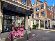Rosa Fahrrad mit Blumen vor einem Coffeeshop in der Binnen Oranjestraat in Amsterdam, mit traditionellen niederländischen Grachtenhäusern im Hintergrund.