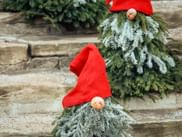 Zwei dekorative Wichtel mit roten Zipfelmützen und Tannenzweig-Bärten auf Steinstufen, die nordische Julfest-Traditionen feiern.