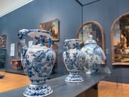 Drei große blau-weiße Delfter Keramikvasen im Rijksmuseum Amsterdam, mit Gemälden an blauen Wänden im Hintergrund.