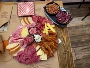 Wooden board with Italian cold cuts, cheese, bread, and fried items. Side dish with roasted chickpeas and red cabbage on rustic table.