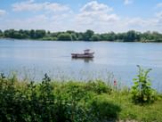 Red and white boat anchored on the Loire River with green vegetation in foreground and tree-lined shore under blue sky with white clouds.