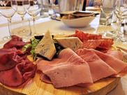 Holzbrett mit italienischen Aufschnittsorten, Prosciutto, Salami und Käse im Hotel Relais Monaco. Weißweingläser und Tischgedeck sichtbar.