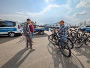 Drei Männer betrachten Fahrräder auf einem Parkplatz mit Eurofun-Servicefahrzeugen und Fahrradanhängern im Hintergrund unter bewölktem Himmel.