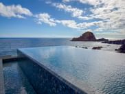 Infinity pool with blue mosaic tiles overlooking the Atlantic Ocean in Porto Moniz, Madeira. Rocky island formation visible in the sea.