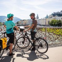 Stopover by two cyclists at the Makartsteg with a view of the old town and fortress of Salzburg