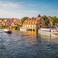 Historische Uferpromenade von Bambergs Klein Venedig mit bunten Fachwerkhäusern entlang der Regnitz und Ausflugsbooten am Ufer.