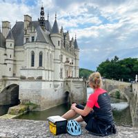 Eine Radfahrerin sitzt auf einer Steinmauer vor dem Schloss Chenonceau an der Loire
