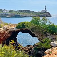 Blick auf Portocolom über Felsformationen am Meer, im Hintergrund der Leuchtturm