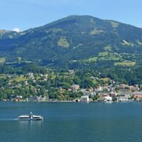 Passagierschiff überquert einen Kärntner See mit einer Stadt am Ufer und grünen Bergen im Hintergrund unter blauem Himmel.