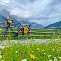 A bicycle stands in front of a pasture fence with a flower meadow in the foreground and the Lienz Dolomites in the background