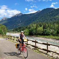 Radfahrerin entlang des Flussen, mit Bergpanorama im Hintergrund