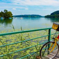 A bicycle stands on a footbridge in Weyerbucht in Mattsee with a view of Schlossberg mountain
