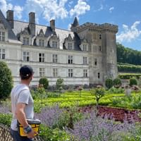 Cyclist with helmet viewing Château de Villandry and its ornamental gardens with colorful flower beds, trimmed hedges, and blue sky.