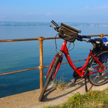 Rotes Fahrrad vor einem Geländer mit Blick auf den See