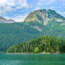 Der Schwarze See mit einer bewaldeten Insel und Bergen im Hintergrund