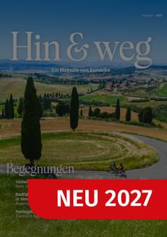 Magazin-Cover mit toskanischer Landschaft mit Zypressen und kurvenreicher Straße. Zwei Radfahrer fahren durch Hügellandschaft. Titel 'Hin & weg' mit rotem Banner 'NEU 2027'.