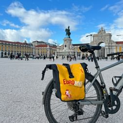 Fahrrad mit gelber Eurobike-Tasche am Praça do Comércio in Lissabon. Der Platz zeigt gelbe Gebäude, eine Reiterstatue und einen Triumphbogen.