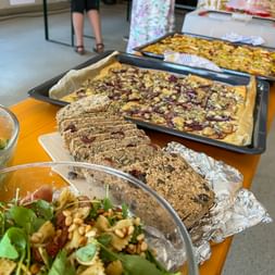Buffettisch mit herzhaften Kuchen, geschnittenem Brot mit Samen, Nudelsalat mit Kräutern und verschiedenen Gerichten bei einem Sommerfest.