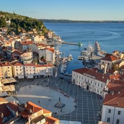 Luftaufnahme von Pirans historischem Stadtzentrum mit roten Ziegeldächern, zentralem Platz, Glockenturm und Hafen an der Adriaküste.