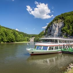 Ausflugsschiff an der Donau beim Donaudurchbruch Weltenburg, mit steilen Kalksteinfelsen und grünen Wäldern unter blauem Himmel.