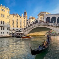 Gondeln auf dem Canal Grande in Venedig mit der historischen Rialtobrücke im Hintergrund, gesäumt von traditionellen venezianischen Gebäuden.
