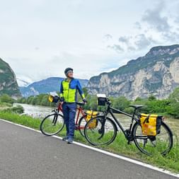 The river Etsch with mountains in the background and the cycle path with cyclists in the foreground