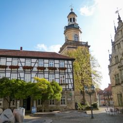 Marktplatz in Rinteln mit Fachwerkhäusern, Kirchturm mit gelber Fassade und verziertem Renaissance-Rathaus unter blauem Himmel.