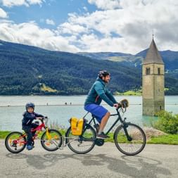 Vater und Sohn radeln vorbei am versunkenen Kirchturm vom Reschensee