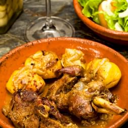 Traditionelles portugiesisches Fleischgericht mit goldenen Kartoffeln in einer Terrakotta-Schale, begleitet von frischem Salat und eingelegtem Gemüse.