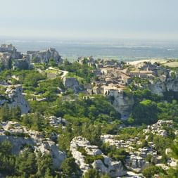 Les Baux-de-Provence, ein historisches Steindorf auf Felsenklippen mit Burgruinen, umgeben von grüner Vegetation und Ebenen in der Provence.