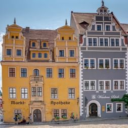 Colorful Renaissance buildings on Meissen market square. Yellow Markt-Apotheke and gray Weinhaus Schuh with ornate gables under blue sky.