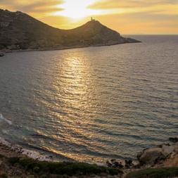 Sonnenuntergang über dem Golf von Gökova mit Leuchtturm auf felsiger Halbinsel. Goldenes Sonnenlicht spiegelt sich auf ruhigem Wasser.