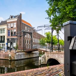 Traditionelle niederländische Zugbrücke über einen Kanal in Schiedam mit historischen Backsteingebäuden und einer Steinbogenbrücke.