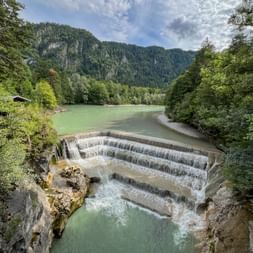Stufenwehr am Lechfall mit türkisfarbenem Wasser, das über mehrere Ebenen fließt, umgeben von Wald und Bergen im Allgäu.