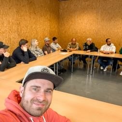 Group selfie of team members seated at U-shaped tables in a wood-paneled room during a Training Days 2026 meeting.