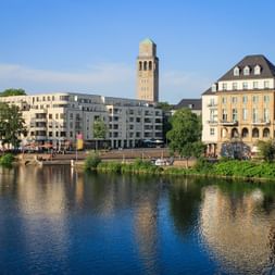 Waterfront view of Mülheim an der Ruhr showing modern apartments, historic brick tower, and traditional buildings reflected in the river.