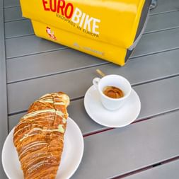 Crossaint mit Esspresso und gelber Lenkertasche im Hintergrund