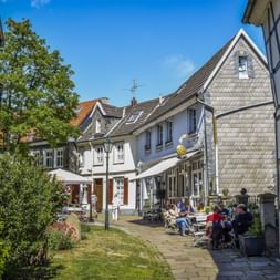Charming cobblestone square in Hattingen's old town with traditional half-timbered houses, outdoor restaurant seating, and visitors enjoying the sunny day.