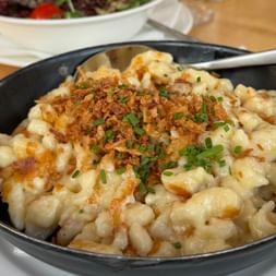Black pan filled with Käsnocken, Austrian cheese dumplings topped with crispy fried onions and fresh chives on a wooden table.