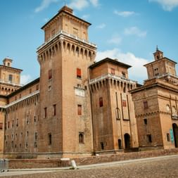 Castello Estense in Ferrara, eine mittelalterliche Backsteinburg mit hohen Türmen und Zinnen unter blauem Himmel mit weißen Wolken.
