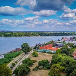 Luftaufnahme des Donauufers in Belgrad mit bunten Gebäuden, grünen Bäumen und dem breiten Fluss unter blauem Wolkenhimmel.
