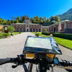 Fahrrad mit Kartenhalter vor dem historischen Gebäude der Alten Saline in Bad Reichenhall, mit Bergen im Hintergrund.