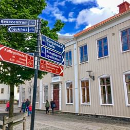 Blue and red cycling direction signs in Kungsbacka showing routes to Resecentrum, Sjukhus, and Kattegattleden. White wooden buildings in background.