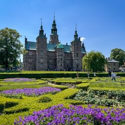 Rosenborg Castle in Copenhagen with ornamental baroque garden featuring purple flowers and geometric hedges under blue sky.