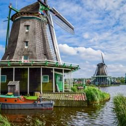 Traditionelle niederländische Windmühlen entlang eines Wasserwegs in Kinderdijk. Eine grüne Windmühle mit weißen Flügeln steht neben einem Kanal.